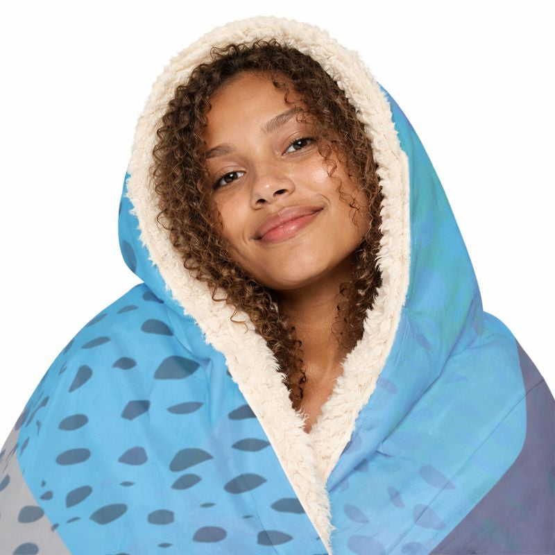 A person with a cream-lined blue patterned blanket hood pulled around their face.