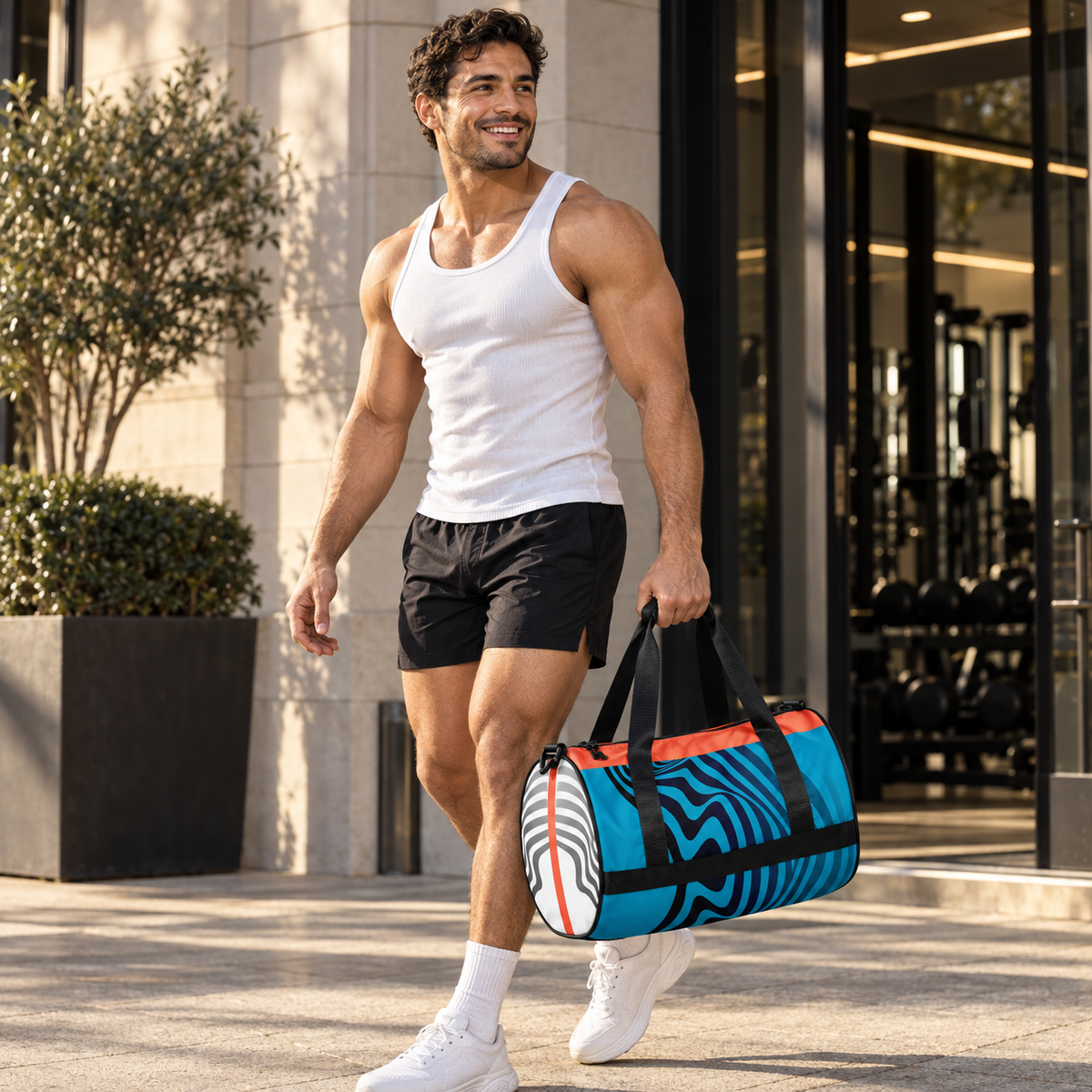 A person in a white tank top and black shorts carrying a blue, coral, black, and white Hot Circuit gym duffle bag outside a gym.