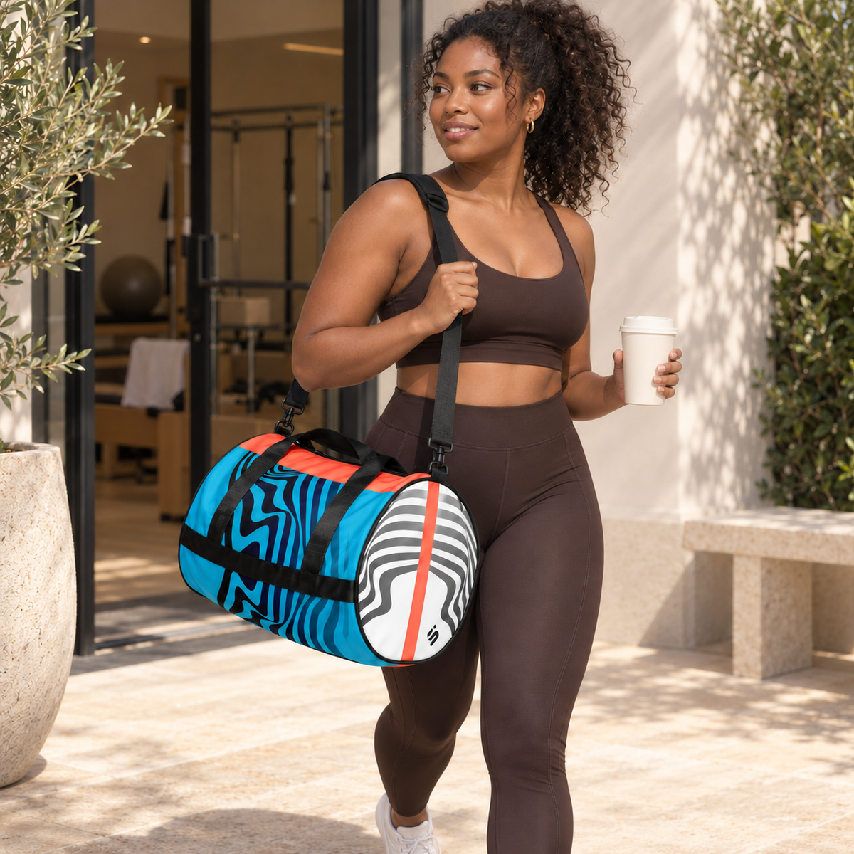 A person in black activewear carrying the Hot Circuit gym duffle bag and a drink outside a gym.