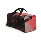 Left-front view of a burgundy, black, and coral geometric duffle bag with black handles and shoulder strap.
