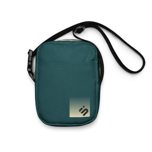 Front view of the dark teal No Reception crossbody bag with a pale yellow monogram patch and black strap.
