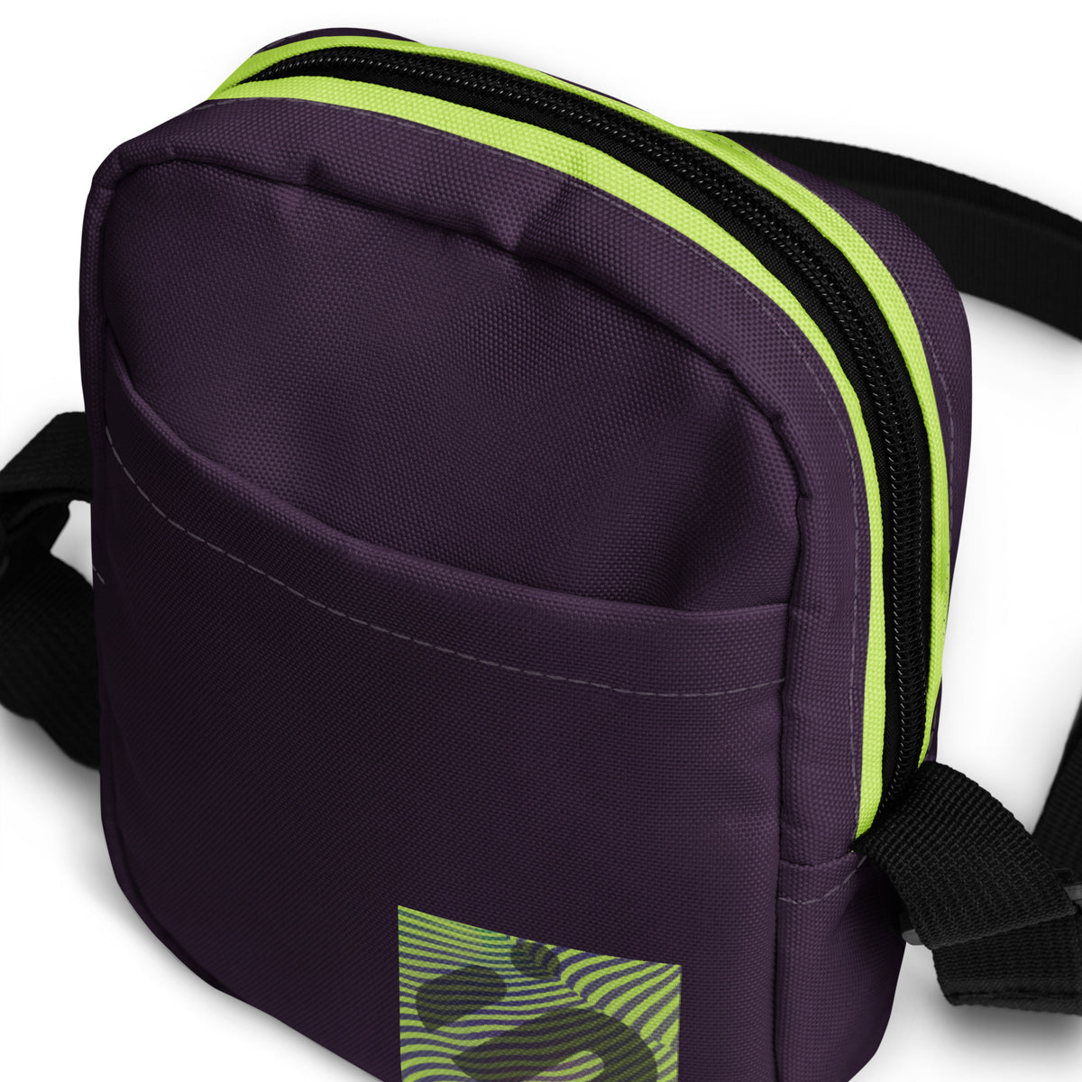 Close-up of the Velvet Detour bag showing its purple front pocket, striped monogram patch, and yellow-green zipper trim.
